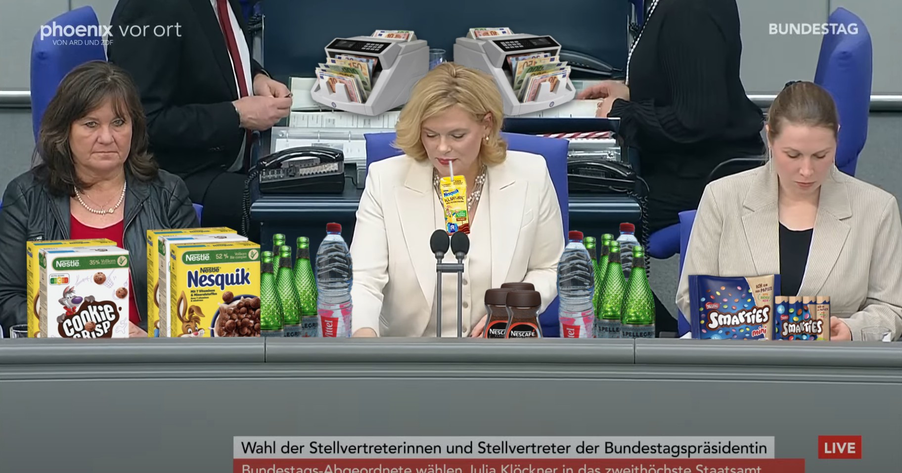 Julia Klöckner im Plenarsaal des Bundestags. Sie sitzt auf ihrem Platz als neue Bundestagspräsidentin. Überall im Bild sind Produkte von Nestle (nachträglich) eingefügt: Nesquik Cornfalkes, Cookie Crisp, Smarties, Nescafe und Wasser von S.Pellegrino und Vittel. In ihrem Mund hängt ncoh ein Trickpäckchen Nesquik-Kakao. Hinter ihr stehen zwei Geldzählmaschinen auf den Tischen.