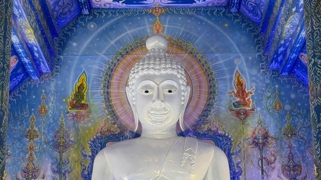 Giant White Buddha statue in front of of painted mural.