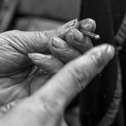 Close up black and white photograph of a man’s hand holding a small metal cylindrical part. The hand is shiny with machine oil.