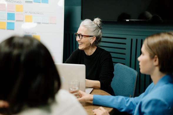  A woman speaks to her colleagues in a modern meeting room, engaging them in discussion around a conference table.