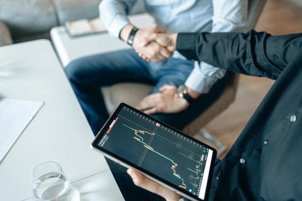 Two individuals shaking hands while standing over a tablet computer, symbolizing collaboration and agreement