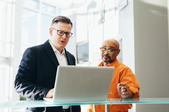  Two men in business suits stand beside a laptop, engaged in discussion or collaboration
