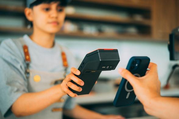 A woman engages with a mobile payment terminal, holding her phone in one hand