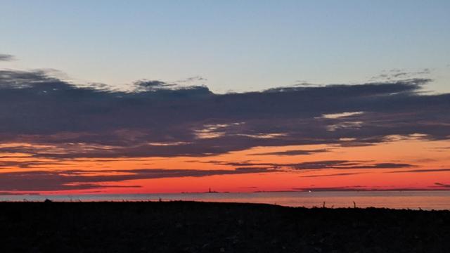 Historical Documentation in the form of a photograph of a rising sun over the ocean bay at Yirrell Beach in Winthrop, MA.  The sky is filled with vibrant colors of orange, pink, and purple, with a few wispy clouds scattered across the horizon. The sun is rising on the horizon, casting a warm glow over the water. In the distance, there is a small island in the distance. The horizon line is visible, with the ocean stretching out in front of it. The overall mood of the image is peaceful and serene.