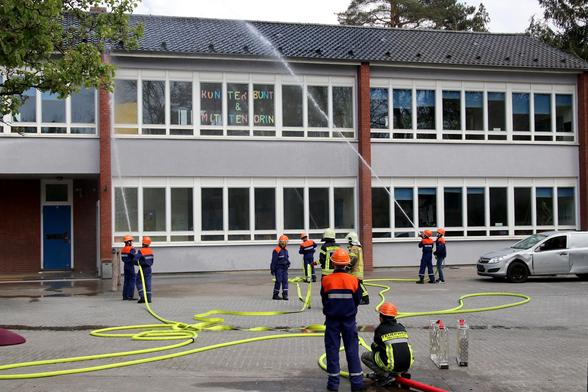 Das Bild zeigt einen Löschzug der Jugendfeuerwehr bei einer Übung während des Tags der offenen Tür. Zwei Angriffstrupps mit C-Rohr 'löschen' ein Schulgebäude.