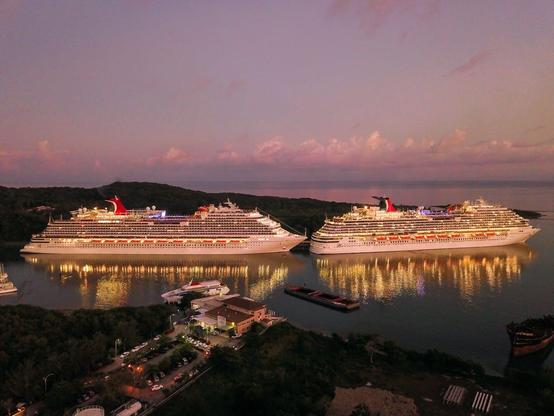 At dusk, two cruise ships are moored at a dock, surrounded by a serene atmosphere and a vibrant sunset sky