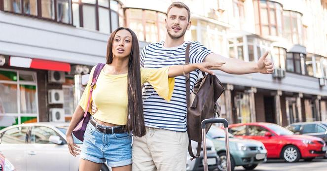 A man and woman stand on the street, arms outstretched, appearing to embrace or welcome someone approaching