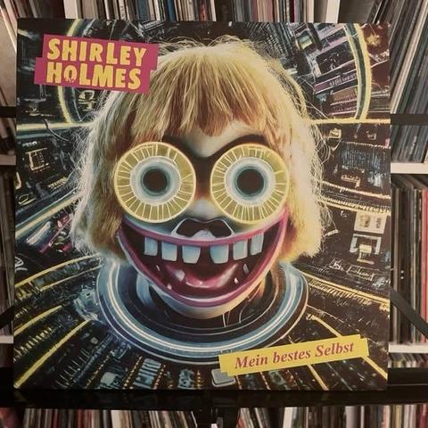 Albumcover mit einem cartoonhaften, übergroßen Gesicht mit leuchtend gelber Brille und einem breiten, grinsenden Mund. Der Hintergrund ist abstrakt und farbenfroh, mit digitalen Elementen. Der Text enthält "SHIRLEY HOLMES" und "Mein bestes Selbst".