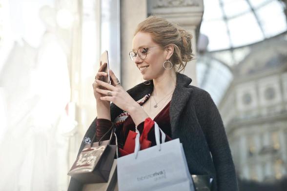  woman holding shopping bags while looking at her phone, appearing engaged and focused on her device