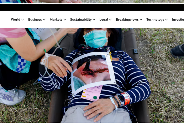 A masked woman is laying on a stretcher with a colour photo of a shrapnel in the back and a person taking her temperature. 