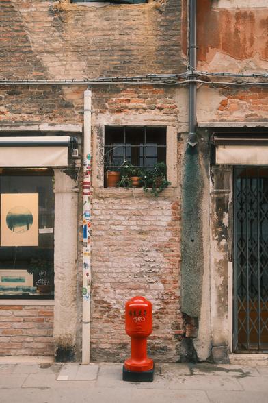 A red fire hydrant in front of weathered brick wall with a window with plants in Venice