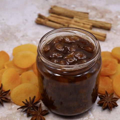 An open jar of apricot chutney next to some dried apricots. 