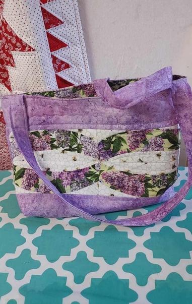 a tote bad, it is a lavender purple color with wavy green and white strips of fabric and purple handles on it 