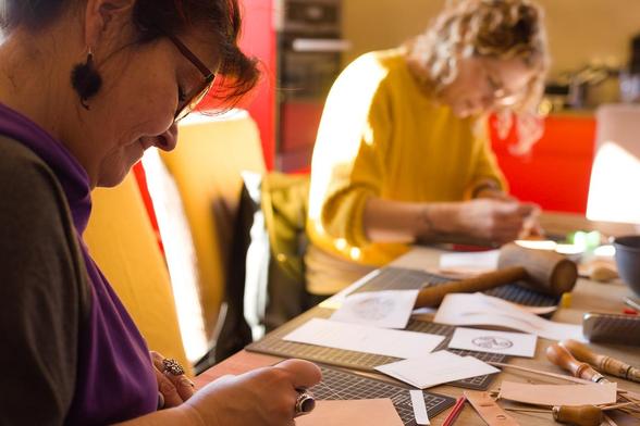 Photo shows two of my students sitting at the workbench and carving images onto the leather. 