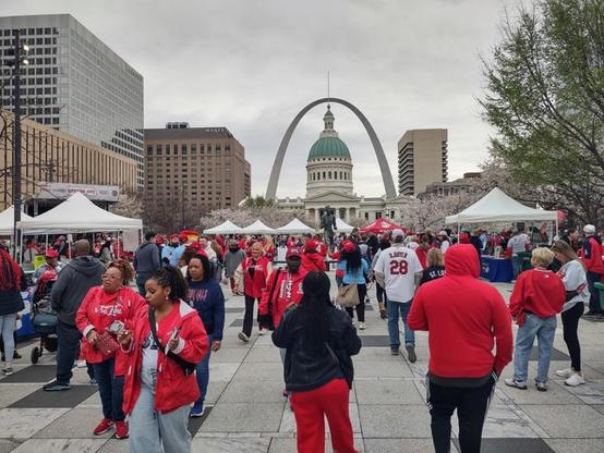 Crowd gathers in downtown Saint Louis, Missouri wearing Cardinal red and white before the Saint Louis Cardinals’ 2025 MLB opening game. The Arch is visible in the background.