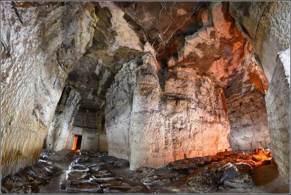 Carrière de gypse souterraine. Un pilier de soutien très massif au centre. Plusieurs sacs en plastique sont posés en rang, au sol. Il s'agit d'anciennes cultures de champignons.