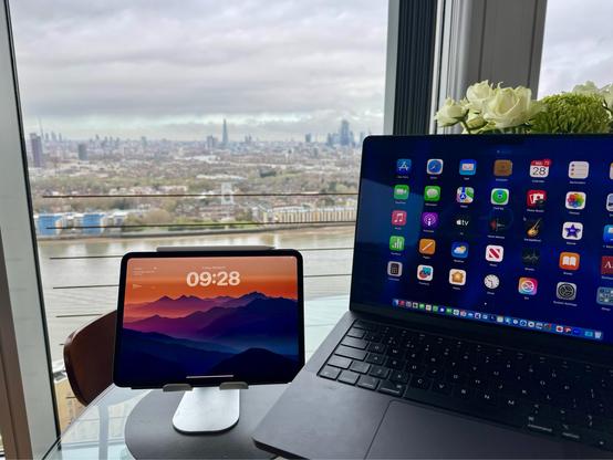 A view of the London skyline, taken from a high-rise apartment block in Canary Wharf. In the foreground, laptop and iPad, in the background, London’s Shard building and a bank of clouds.