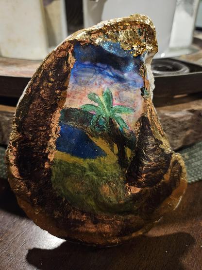 Photo of an oyster shell with an island scene. It is accented with gold leaf.