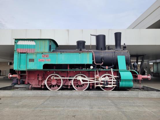 Old steam locomotive painted green, red and black in front of the train station.