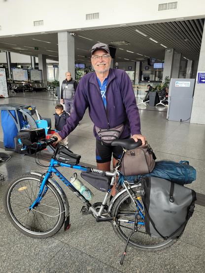 Bob, smiling, and his mountain bicycle full of panniers in the station building.