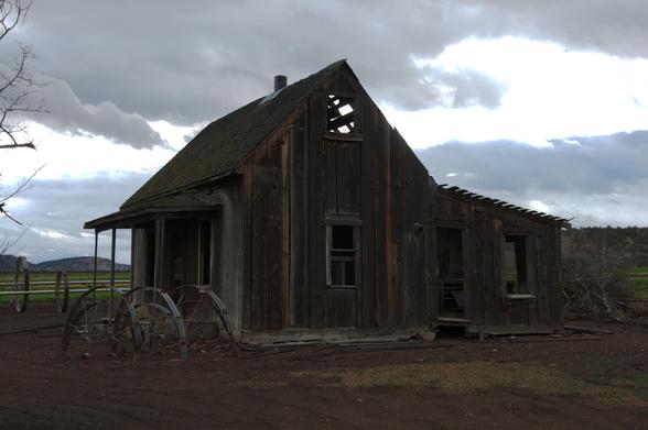 Sideview of abandoned farmhouse with clouds in background
