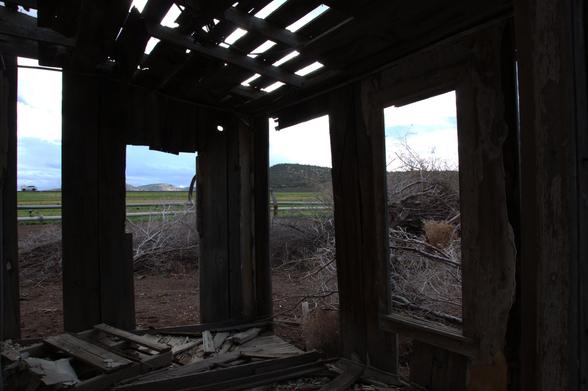 View from out the back windows of the farmhouse. Roof falling apart, windows gone, farmland in background