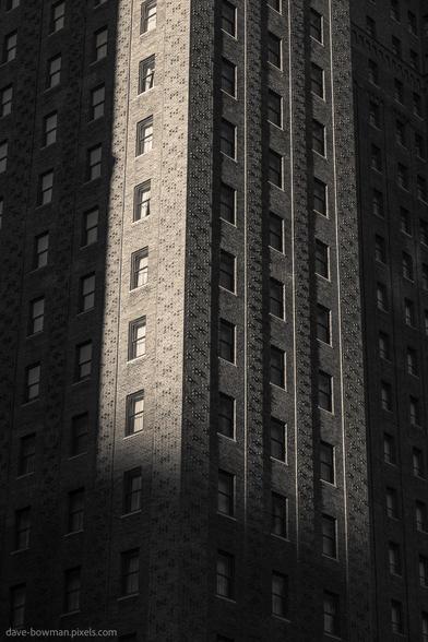 A photograph of the historic Allerton Hotel in Chicago, taken in late afternoon, showcases a section of its iconic architecture in monochrome. The interplay of light and shadow emphasises the building’s details, with strong contrasts accentuating its structure and design.