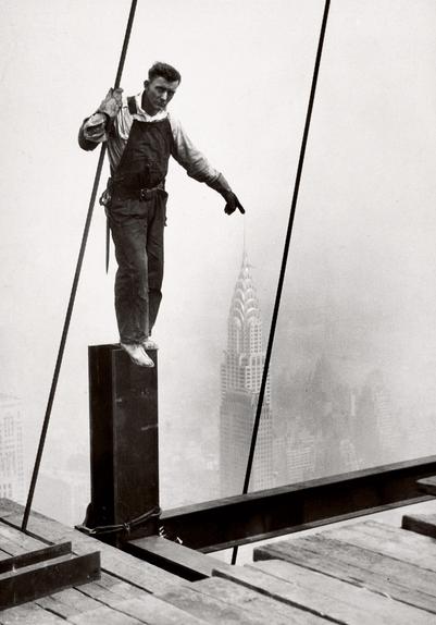 Iron worker in New York City standing on a piece of wide flange with his finger perspectively touching the tip of the Empire State building spire 