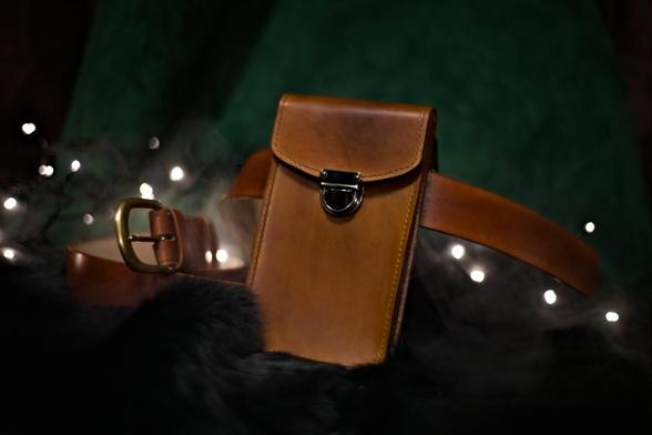 This is a photo of medium brown leather belt bag suitable for a smaller item like a phone. Leather belt bag on the front side. Photo depicts how it would look if the bag was worn vertically on the belt. 