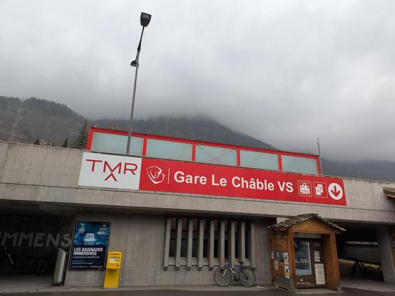 Gare de Le Châble d'extérieur, bâtiment en béton. Ciel gris, il pleut