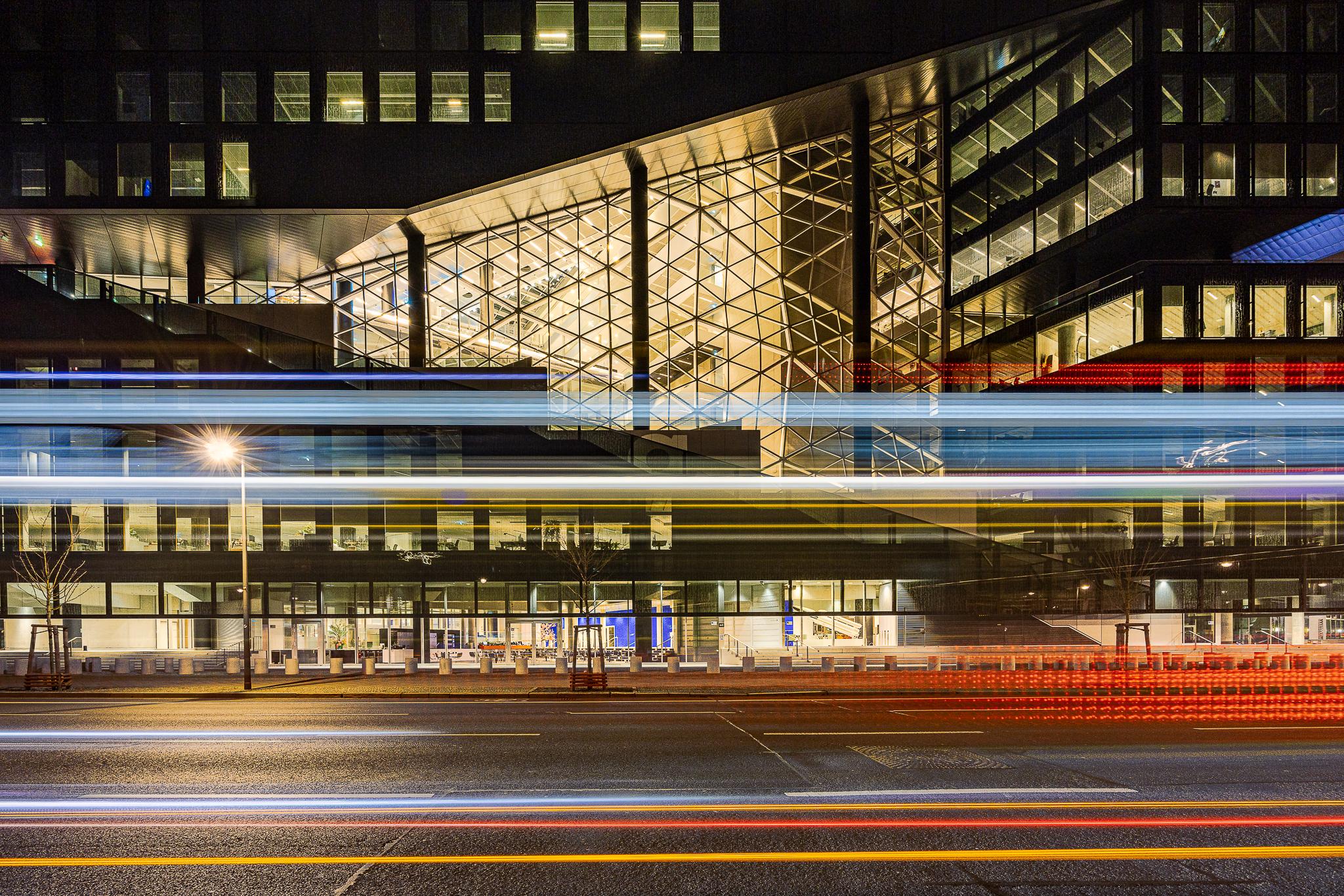 Long exposure shot at night of a bus passing in front of the modern Springer building in Berlin. Only the lights of the bus are visible and add an abstract look to the chaotic shape of the building behind. Long exposure shot at night of a bus passing in front of the modern Springer building in Berlin. Only the lights of the bus are visible and add an abstract look to the chaotic shape of the building behind.