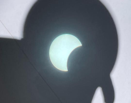 Partial solar eclipse projected through binoculars onto a sheet of white card
