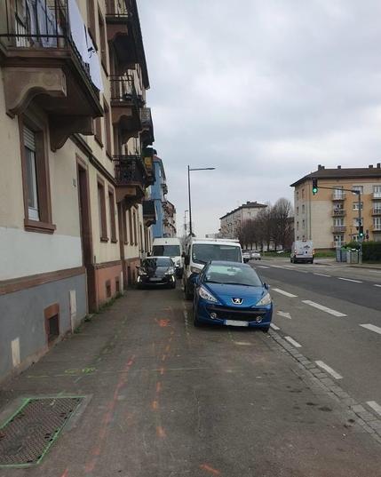 Une Citroën DS3 et une camionnette blanche stationnés l’un derrière l’autre sur le trottoir route d’Oberhausbergen, tandis qu’une autre file de 3 voitures est stationnée à côté d’eux sur des emplacements de stationnement matérialisés sur le trottoir. Ça ne laisse aucune place pour les piétons pour passer. A côté, la route d’Oberhausbergen est très large et déserte.
