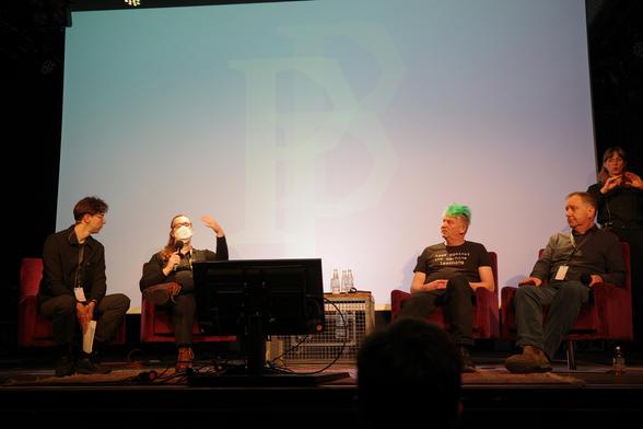Photo of four people on chairs on a stage