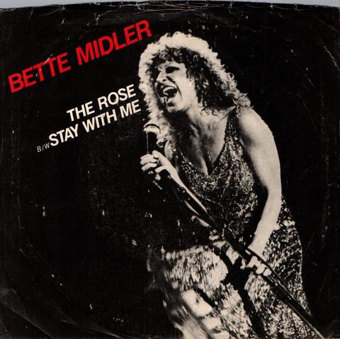 This is the front cover of the 45 RPM single of music artist, Bette Midler's song, "The Rose". It's a black and white photo with her name in red. It lists "THE ROSE" and also the B-side "STAY WITH ME".