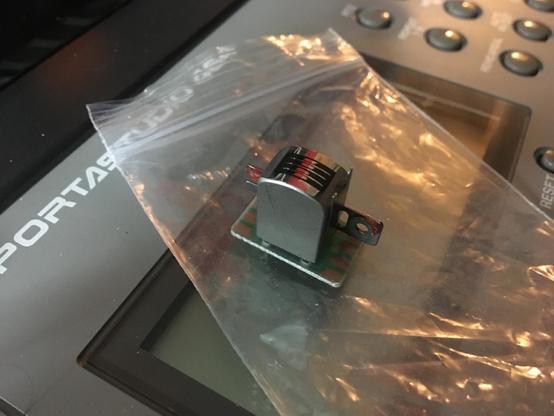 A close-up of a record/playback tape head before it was installed in a Tascam 464 multitrack cassette recorder. The head sits on top of a plastic bag, which itself rests on the LCD screen of the 464 unit.