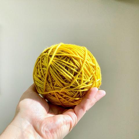 A yellow ball of yarn, glowing in the sunlight, is held up against a white background.