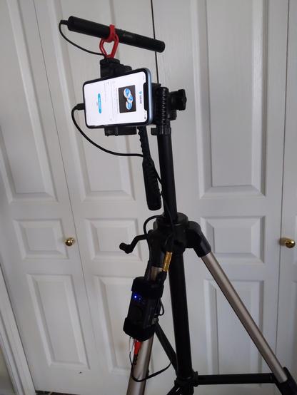 A tripod with an iRig mounted to one leg, connected to a stereo microphone which is mounted above an iPhone XR.