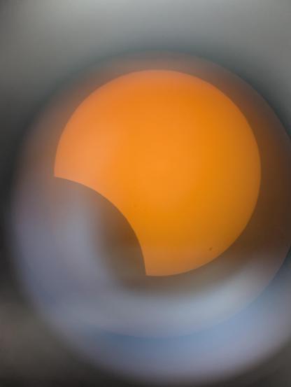 Foto durch das Okular eines Teleskops: es ist die partielle Sonnenfinsternis zu sehen. Der Mond verdeckt ca 15% der Sonnenscheibe.