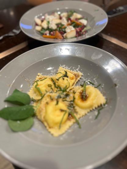 Brown butter ravioli in a bowl with the salad behind it. 
