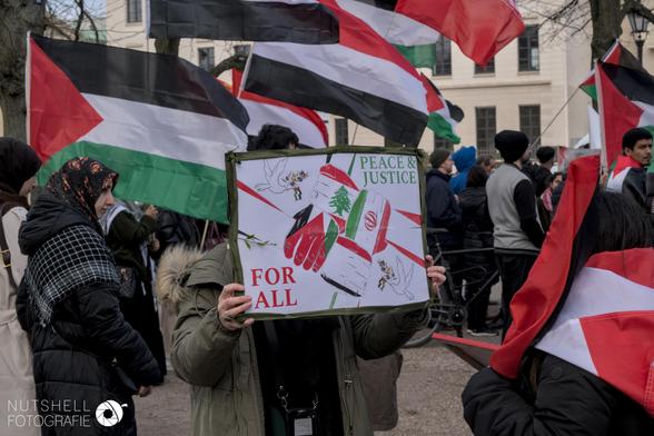 Ein Schild mit vier in sich greifenden Fäusten in den Farben der Flaggen von Jemen, Libanon, Palästina und dem Iran.