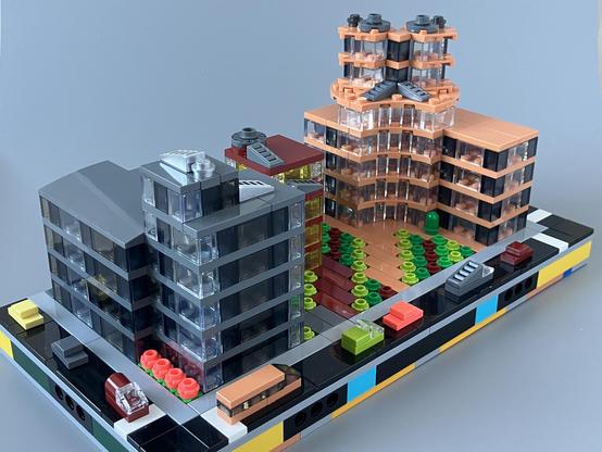Front left three quarter view with a 4-6 storey dark grey building dominating the foreground  