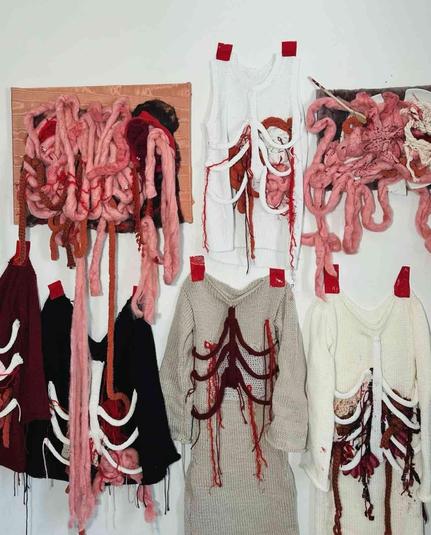 Knitted garments with incorporated anatomical elements, including intestines, ribs, and other organic forms, displayed on a wall.