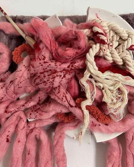 Close up of an abstract wall hanging of tangled, pink and red dyed wool threads representing intestines.
