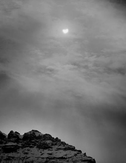 A black and white picture of a partial solar eclipse. At the bottom of the picture is a top of a snowy mountain.