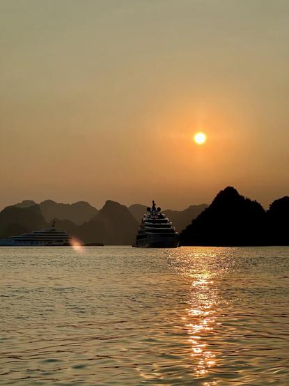 Puesta de sol en la Bahía de Ha Long con unos barcos y las montañas al horizonte.