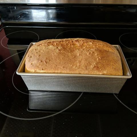 The baked loaf of bread still in the pan, it is golden brown or so..