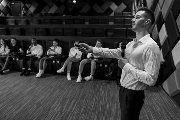 A man delivers a presentation to a captivated crowd, gesturing confidently in a professional setting