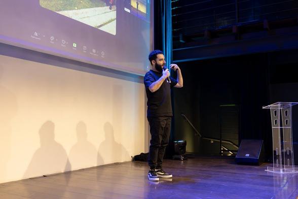 A man with a microphone stands on stage, engaging with the audience during a presentation