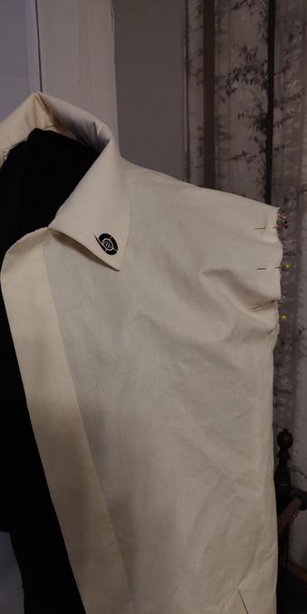 A sand colored jacket with pinned in sleeve and Bernadelli Communications logo on the collar on a dressform.
